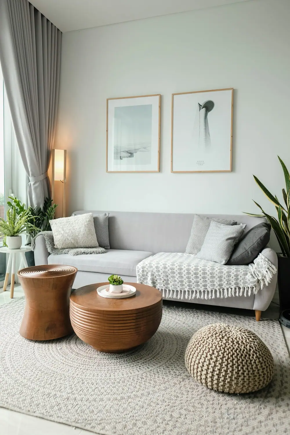 Sala de apartamento clara, com sofá cinza, plantas e mesas de madeira.