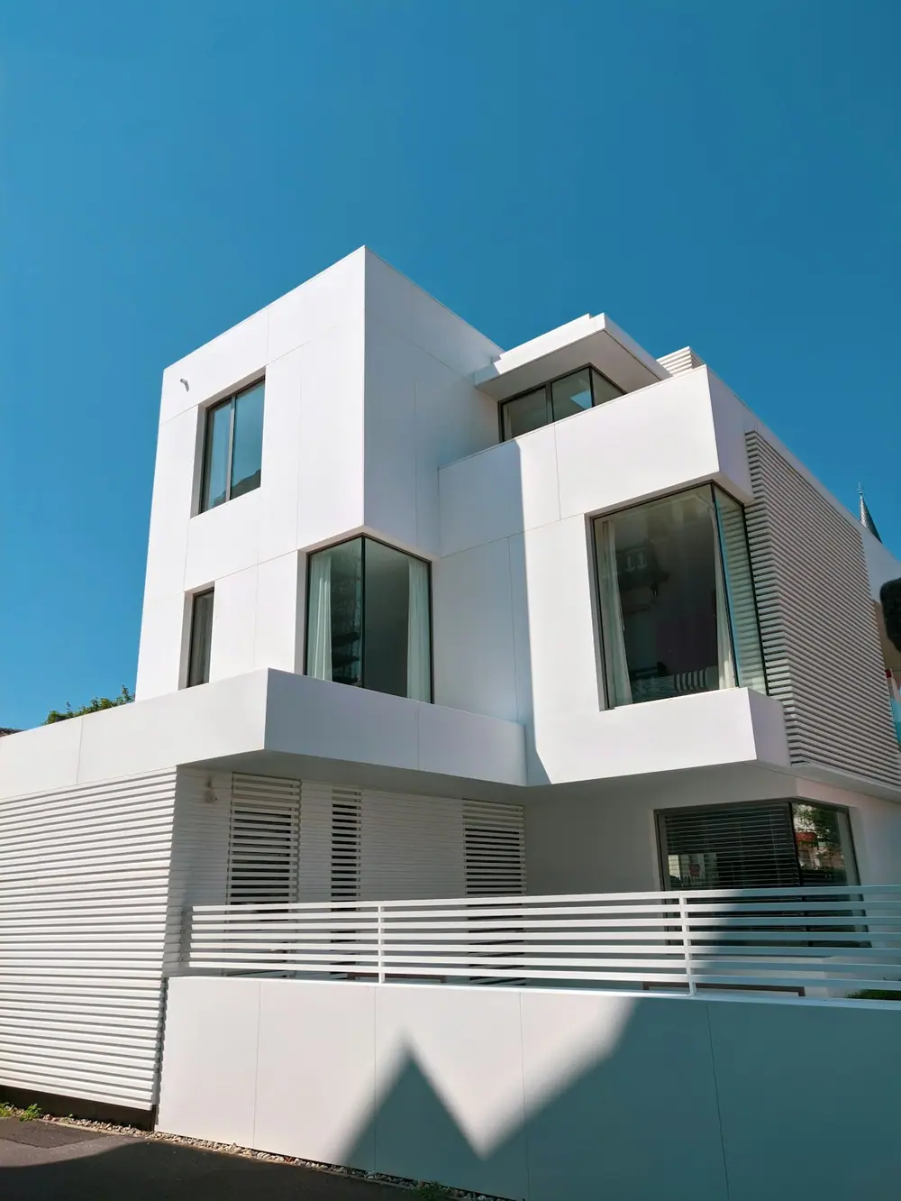 Fachada branca de uma casa contemporânea sob o céu azul.